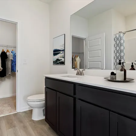Modern bathroom with dark wood vanity, white countertop, and adjacent walk-in closet with hanging clothes.