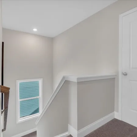 Bright landing area at top of stairs with beige walls, white trim, and closed white door.