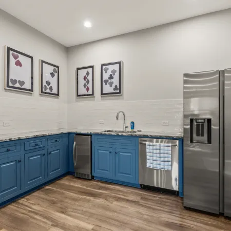 Modern kitchen with blue cabinets, stainless steel appliances, wooden flooring, and playing card art on white walls.