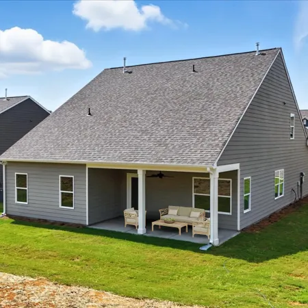 Modern gray house with a covered patio and outdoor furniture on a sunny day with green lawn.