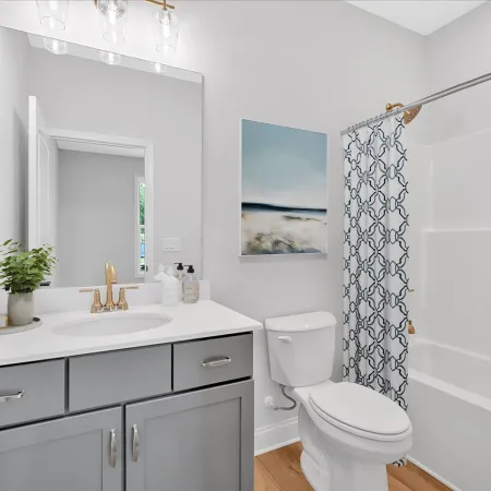 Modern bathroom with gray vanity, white countertop, toilet, patterned shower curtain, and wall art.
