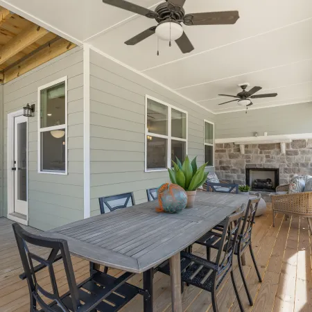 Spacious screened porch with wooden flooring, dining table, chairs, ceiling fans, and stone fireplace.