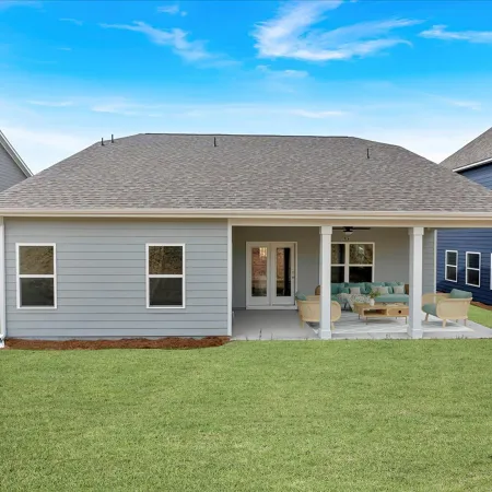 Modern gray single-story house with covered patio and outdoor seating in a green lawn backyard.