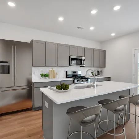 Modern kitchen with gray cabinets, stainless steel appliances, white island countertop, and bar stools under recessed lighting