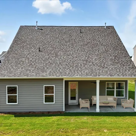 Single-story gray house with a large covered patio and lawn under a blue sky with clouds.