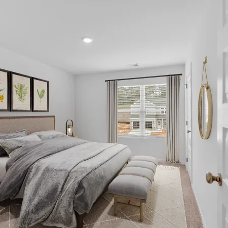 Cozy modern bedroom with gray bedding, wooden furniture, botanical wall art, and a window with beige curtains.