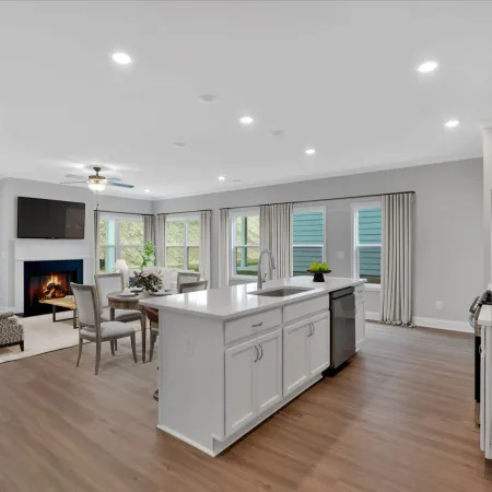 Open concept kitchen and living room with white cabinets, hardwood floors, fireplace, and large windows.
