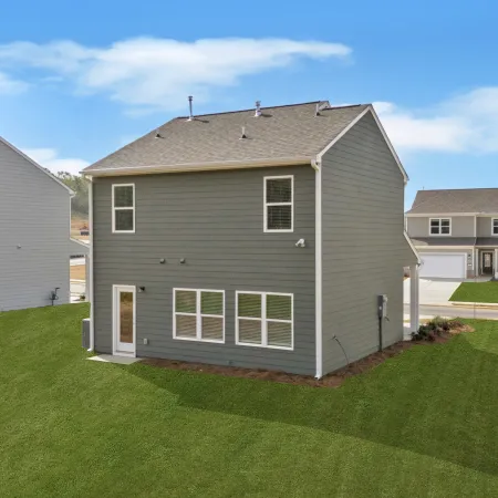 Modern two-story green house with a large yard, surrounded by neighboring homes and blue sky.