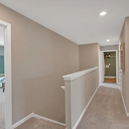 Bright and spacious hallway with light-colored walls and carpet, leading to rooms.
