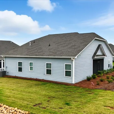 New modern suburban house with gray siding and landscaped yard under blue sky with clouds.