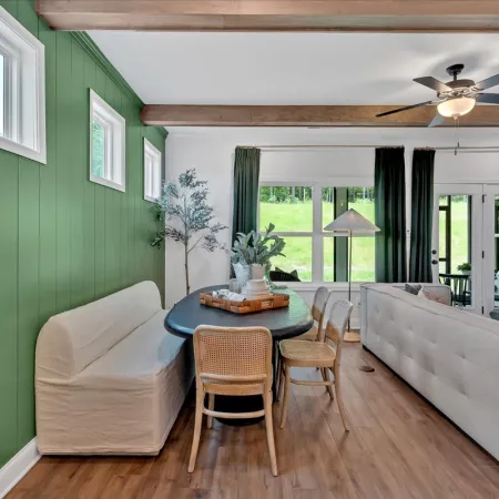 Cozy dining nook with green paneled wall, beige bench, wooden chairs, and a black oval table in an open living space.