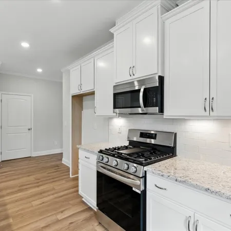 Modern kitchen with white cabinets, granite countertops, stainless steel stove and microwave, and wood flooring