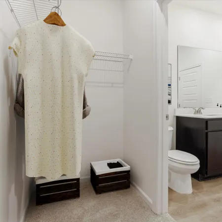 White speckled dress hanging in a walk-in closet with dark storage bins visible next to a bathroom vanity.