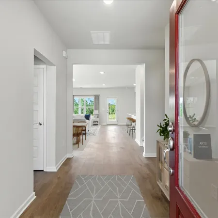View through an open red door into a modern bright home with wood floors and natural light from windows.