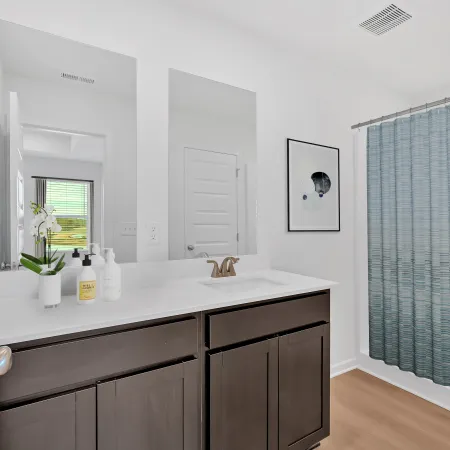 Modern bathroom with dark wood vanity, white countertop, dual mirrors, and blue shower curtain on wooden floor