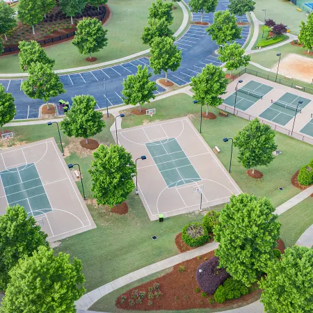 Aerial view of a park with basketball courts, tennis courts, walking paths, and landscaped greenery on a sunny day.