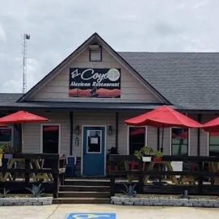 Exterior view of El Coyote Mexican Restaurant with red umbrellas and outdoor seating under cloudy sky.