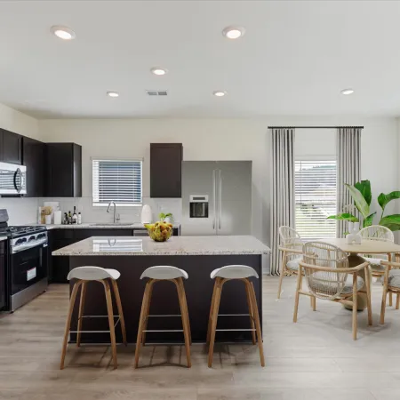 Modern open kitchen with island, three barstools, stainless steel appliances, and a dining area with round table and chairs.