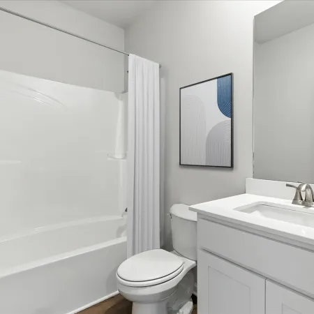 Modern bathroom with white bathtub, toilet, vanity with sink, large mirror, and abstract wall art.