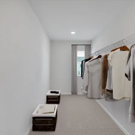 Minimalist walk-in closet with hanging clothes on wire rack, white walls, carpet floor, and window at the end.