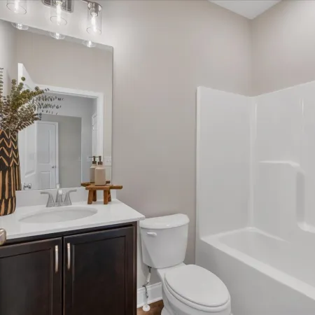 Modern bathroom with dark wood vanity, white countertop, toilet, and white bathtub with shower.