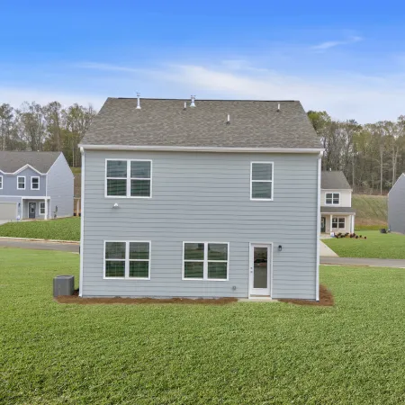 Back view of a modern two-story gray house with a spacious lawn and bright blue sky.