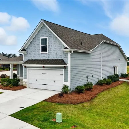 Modern two-story gray house with a garage, landscaped front yard, and a clear blue sky background.