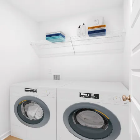 White laundry room with front-loading washer and dryer, wire shelf holding towels and bottles above appliances.