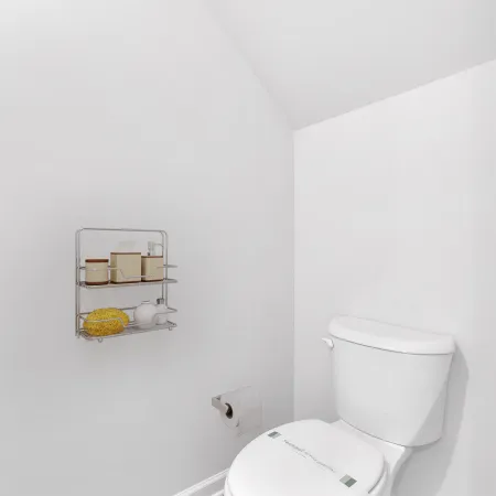 White toilet in a minimalist bathroom corner with wood flooring and wall-mounted storage shelf.