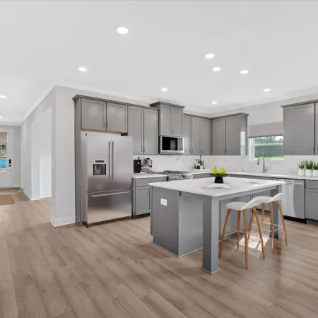 Modern kitchen with grey cabinets, stainless steel appliances, kitchen island with stools, and wood flooring.