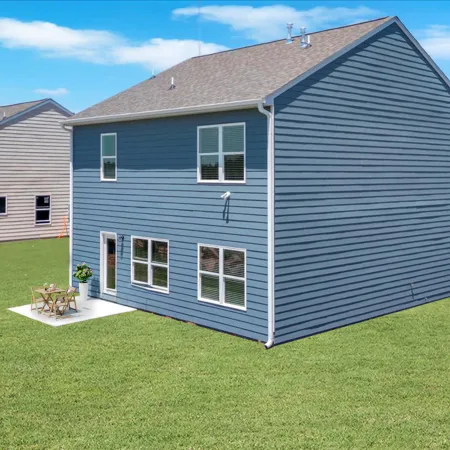Blue two-story house with multiple windows and small patio on large green lawn under clear sky