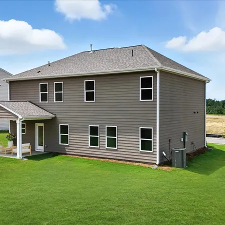 Modern two-story house with gray siding and a covered patio on a spacious green lawn under a blue sky.