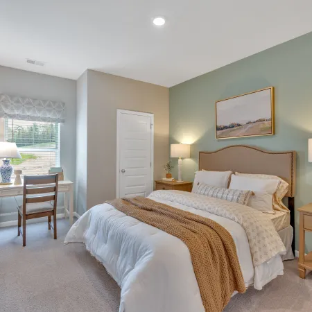 Cozy bedroom with a bed, desk, and natural light, featuring soft colors and stylish decor.