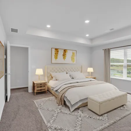 Bright modern bedroom with beige tufted bed, patterned rug, nightstands, lamps, and large window with curtains.