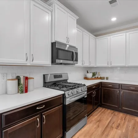 Modern kitchen with white upper cabinets, dark lower cabinets, stainless steel appliances, and wood flooring.
