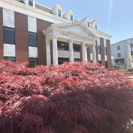 A beautiful courthouse framed by vibrant red foliage under a sunny sky.