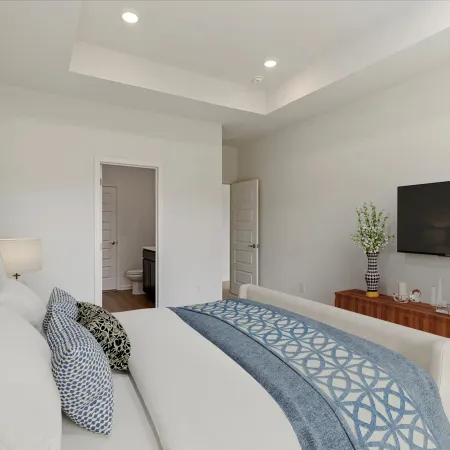 Modern bedroom with white walls, beige bed, blue patterned bedding, wooden TV stand, and bathroom visible through open door.
