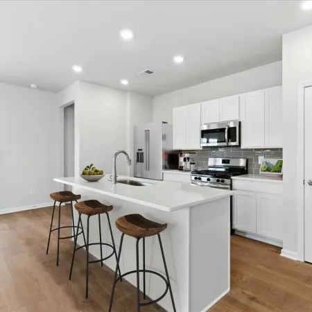 Modern kitchen with white cabinets, stainless steel appliances, island with wooden stools, and wood flooring.
