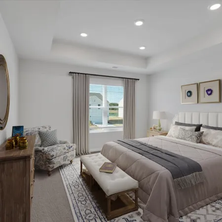 Bright bedroom with beige bedding, patterned armchair, wooden furniture, large window, and decorative wall art.