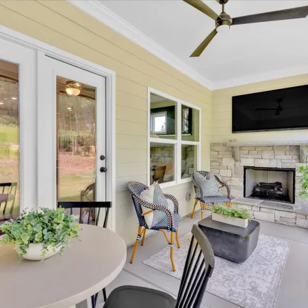 Covered patio with stone fireplace, wall-mounted TV, wicker chairs, round table with plant, and ceiling fan