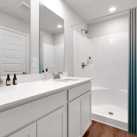 Bright modern bathroom with white vanity, large mirror, walk-in shower, and wood-look flooring