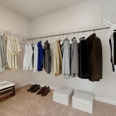 Organized walk-in closet with shirts, jackets, sweaters, shoes, and storage boxes on carpeted floor.