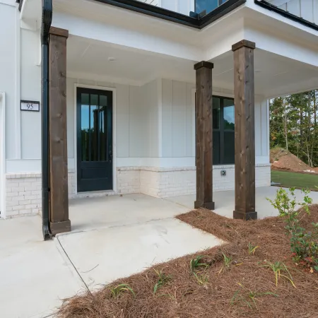 Front porch of modern white house with dark wooden columns and landscaped garden bed.