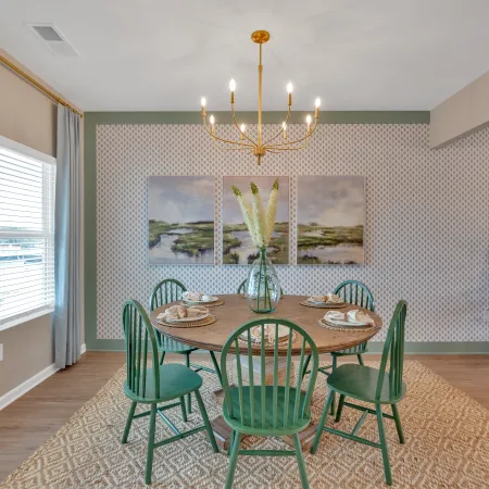 Stylish dining room featuring a round green table, chairs, chandelier, and decorative wall art.