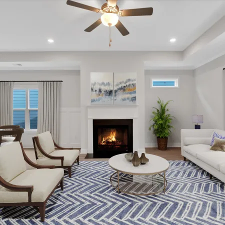 Bright modern living room with white sofa, fireplace, armchairs, round coffee table, and blue patterned rug.