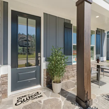 Front porch with dark blue door, stone siding, welcome mat, and outdoor seating with wooden pillars.