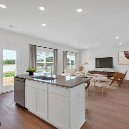 Bright open-concept kitchen and living room with white cabinetry, granite countertops, and modern wood flooring.