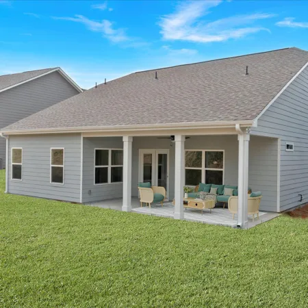 Modern gray house with covered patio, outdoor furniture, and a green lawn under a blue sky.