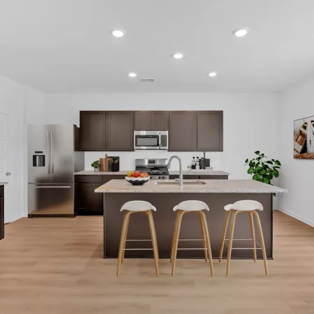 Modern kitchen with dark wood cabinets, stainless steel appliances, an island with three stools, and light hardwood floors.