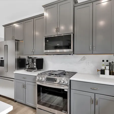 Modern kitchen with gray cabinets, stainless steel appliances, white countertops, and hardwood floors.